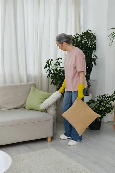 Uma mulher madura espanca o sofá em seu apartamento moderno. — Fotografia de Stock