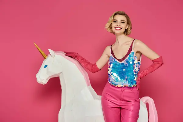 Woman on white unicorn smiles in pink outfit on pink background. — Stock Photo