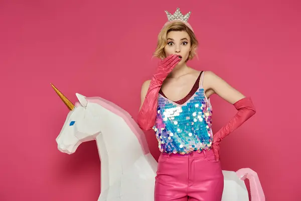 Woman in pink crown and sequined top looks surprised next to white unicorn. — Stock Photo