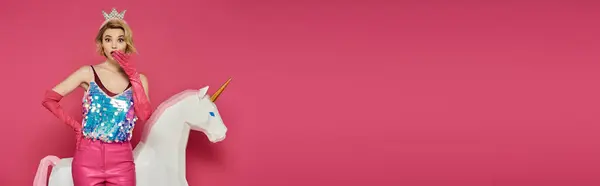 Una mujer con un traje rosa y una corona posa con un unicornio blanco. - foto de stock