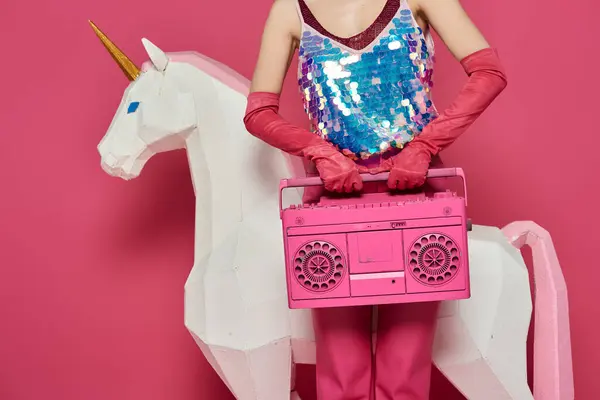 A woman in pink attire holds a pink boombox, standing next to a white unicorn sculpture. — Stock Photo