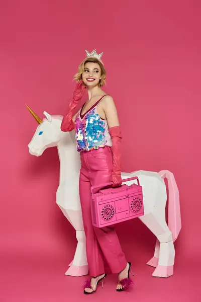 A woman in a pink outfit and a crown poses with a white unicorn and a pink boombox. — Stock Photo