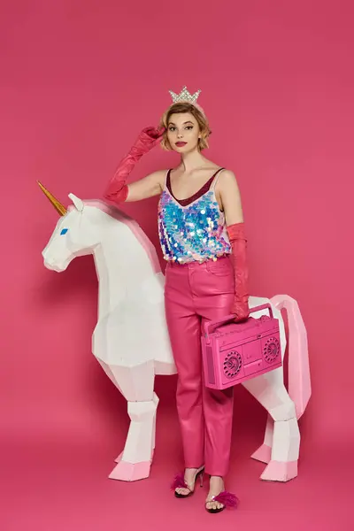 A woman in a pink outfit and a crown poses with a white unicorn and a pink boombox. — Stock Photo