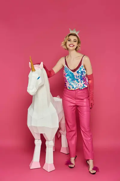 Mujer en traje brillante rosa posa con unicornio blanco sobre fondo rosa. - foto de stock