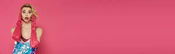 Woman in colorful dress, red gloves, and surprised face against pink background. — Stock Photo