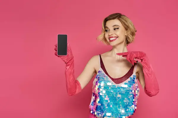 A woman in a sequined top and pink gloves holds a smartphone with a blank screen. — Stock Photo
