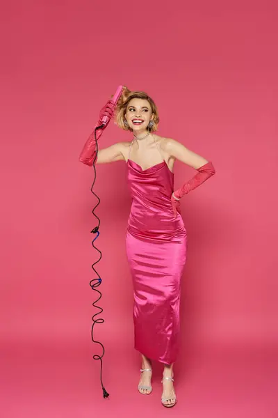 A woman in a pink dress and gloves styles her hair with a curling iron. — Stock Photo