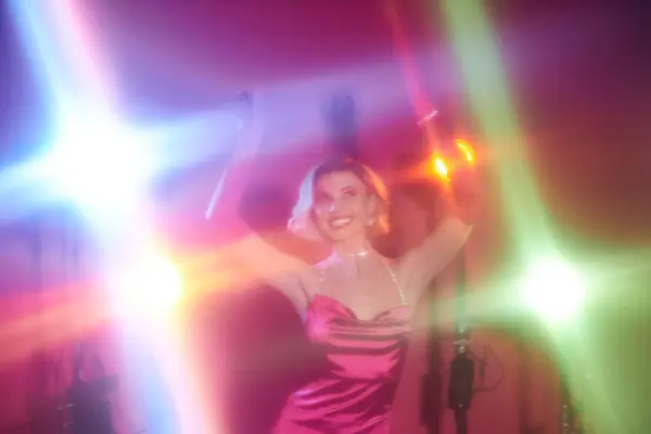 A woman in a pink dress dances under colorful lights. — Stock Photo