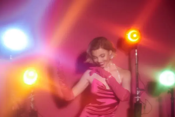 A woman in a vibrant pink dress poses under colorful stage lights. — Stock Photo
