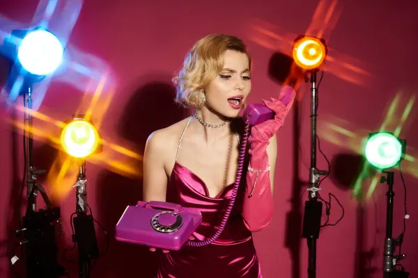 A woman in a pink dress talks on a rotary phone, surrounded by colorful studio lights. — Stock Photo