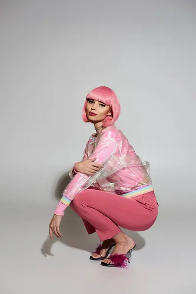 A woman with pink hair sits in a squat pose wearing a transparent pink jacket and matching pants. — Stock Photo