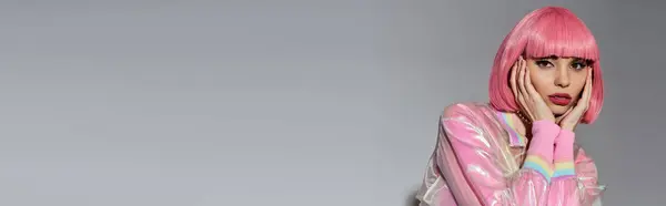 A young woman with pink hair and vibrant pink clothing poses against a grey background. — Stock Photo