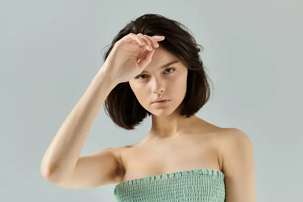 Una donna con i capelli corti e scuri posa su uno sfondo chiaro, con la mano che le protegge gli occhi. — Foto stock