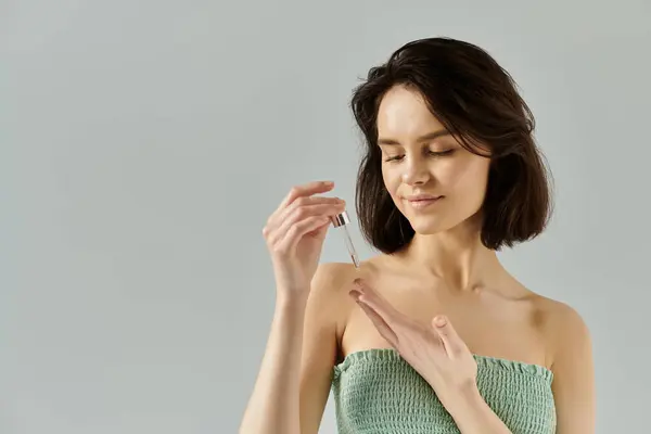 Uma mulher em um top verde aplica soro à sua pele na frente de um fundo cinza. — Fotografia de Stock