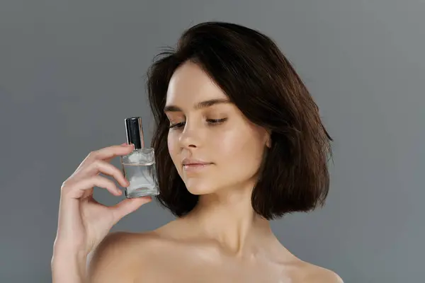 Una mujer hermosa sostiene un frasco de perfume delante de su cara, mirándolo atentamente. — Stock Photo