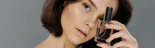 Una giovane donna con i capelli castani tiene una bottiglia di profumo davanti al viso. — Foto stock