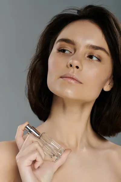 A woman with short, dark hair is spritzing perfume in front of a vibrant backdrop. — Stock Photo