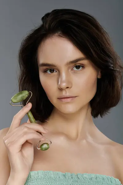 A young woman holds a jade roller, showcasing her natural beauty and a calm demeanor. — Stock Photo