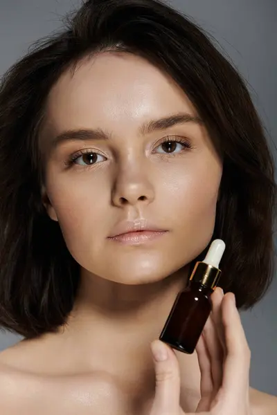A close-up portrait of a woman holding a small bottle of serum, her gaze captivating. — Stock Photo