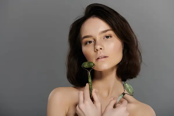 Uma mulher com cabelo escuro curto segura um rolo de jade na frente de um fundo cinza. — Fotografia de Stock