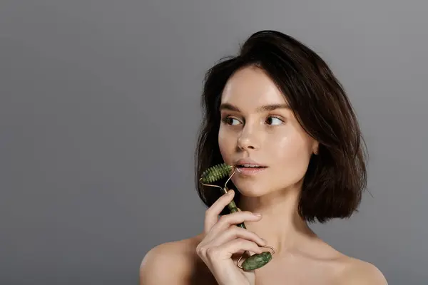 A woman with short brown hair holds a jade roller and looks off to the side. — Stock Photo