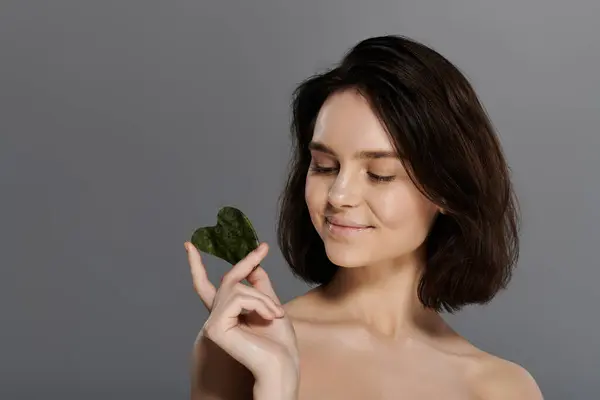 A woman holds a gua sha against a grey background. — Stock Photo
