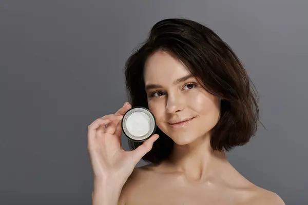 Una mujer con una sonrisa brillante sostiene un frasco de crema, mostrando su piel brillante. - foto de stock
