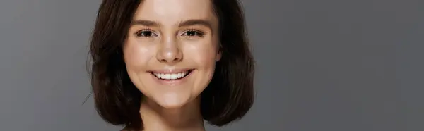 A young woman with dark hair smiles brightly against a plain grey backdrop. — Stock Photo