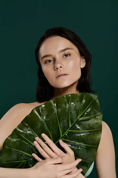 A woman poses with a large leaf against a vibrant green backdrop. — Stock Photo