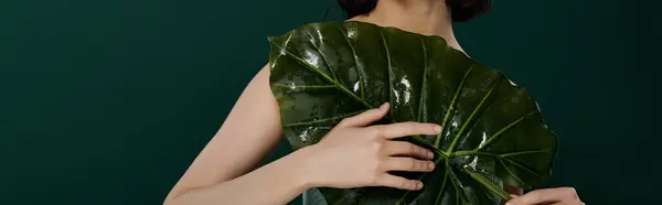 Une femme pose avec une grande feuille humide sur fond vert foncé. — Photo de stock