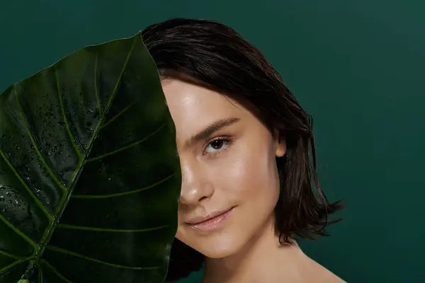 Woman with short dark hair behind a green leaf glows serenely at the camera. — Stock Photo