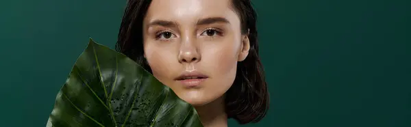 A beautiful woman poses with a large leaf against a vibrant green backdrop. — Stock Photo