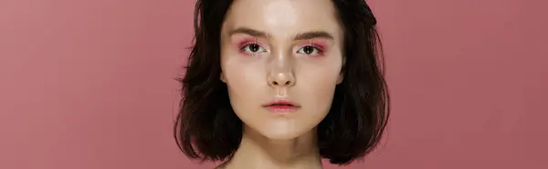 A woman poses against a pink backdrop, her gaze direct and captivating. — Stock Photo