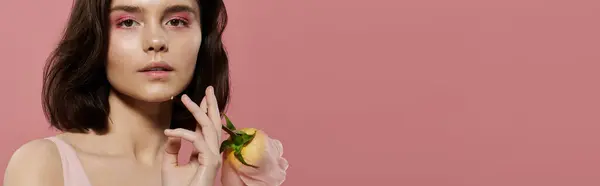 A woman poses with a yellow rose against a pink backdrop. — Stock Photo