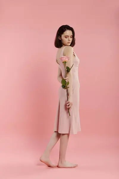Une femme en robe rose tient une rose sur fond rose. — Photo de stock