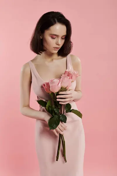 A woman in a pink dress holds a bouquet of roses in front of a bright pink background. — Stock Photo