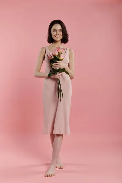 A woman in a pink dress holds a bouquet of roses in front of a pink background. — Stock Photo