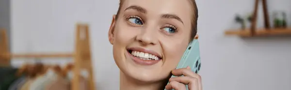 A young woman smiles brightly as she talks on her phone while at home. — Stock Photo