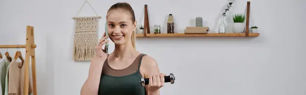 A woman in workout clothes smiles while lifting weights and talking on her phone. — Stock Photo