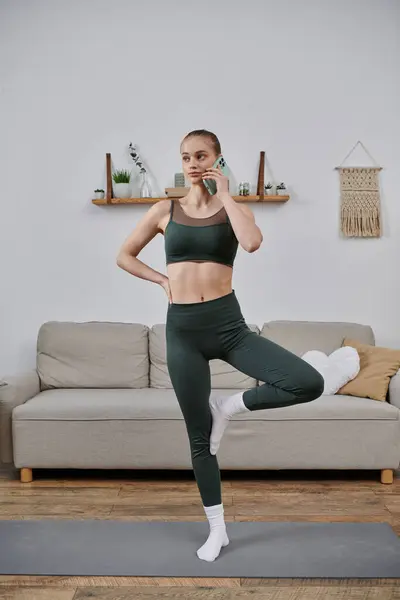 A woman in athletic wear practices yoga at home while talking on the phone. — Stock Photo