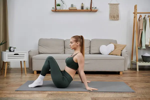 Una giovane donna esegue un esercizio di base su un tappetino yoga nel suo salotto. — Foto stock