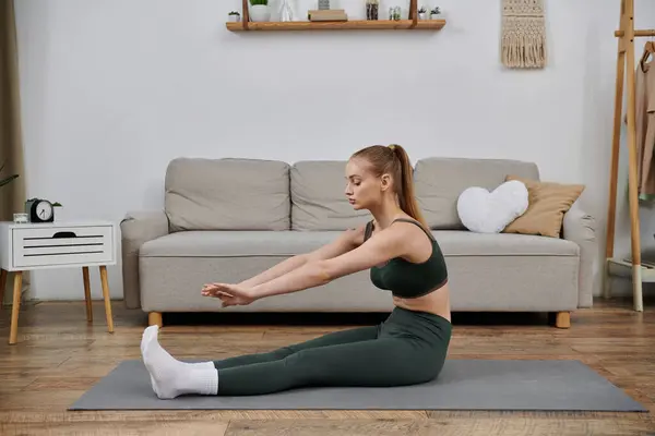 A young woman performs a yoga stretch at home, focusing on her well-being. — Stock Photo