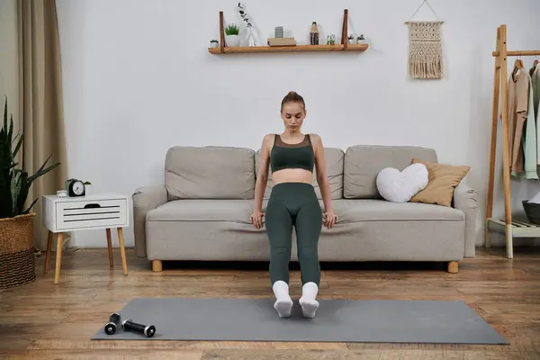A young woman performs an exercise using a couch for support in her living room. — Stock Photo