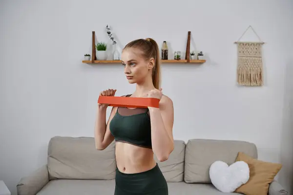 A young woman doing an upper body workout at home with a resistance band. — Stock Photo