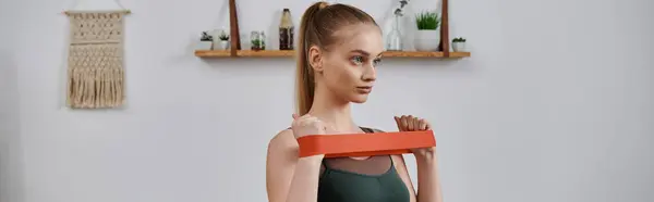 A young woman is working out at home with a resistance band. — Stock Photo