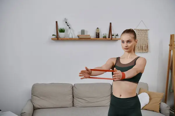A young woman stretches with a resistance band while working out at home. — Stock Photo