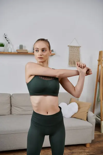 A young woman in athletic wear stretches her arms in her living room. — Stock Photo