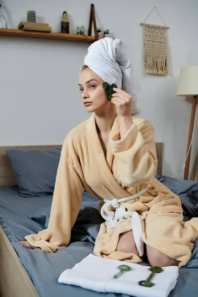 A young woman sits on her bed in a bathrobe, enjoying a relaxing facial at home. — Stock Photo