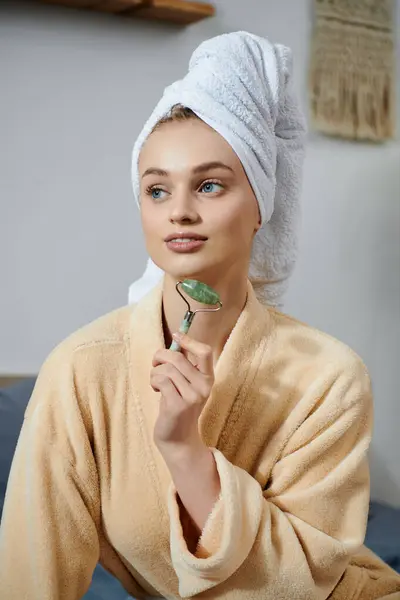 A young woman in a robe uses a jade roller for a self-care routine at home. — Stock Photo