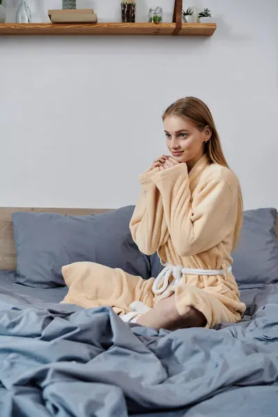 Eine junge Frau im Mantel sitzt auf einem Bett und blickt zur Seite. — Stockfoto